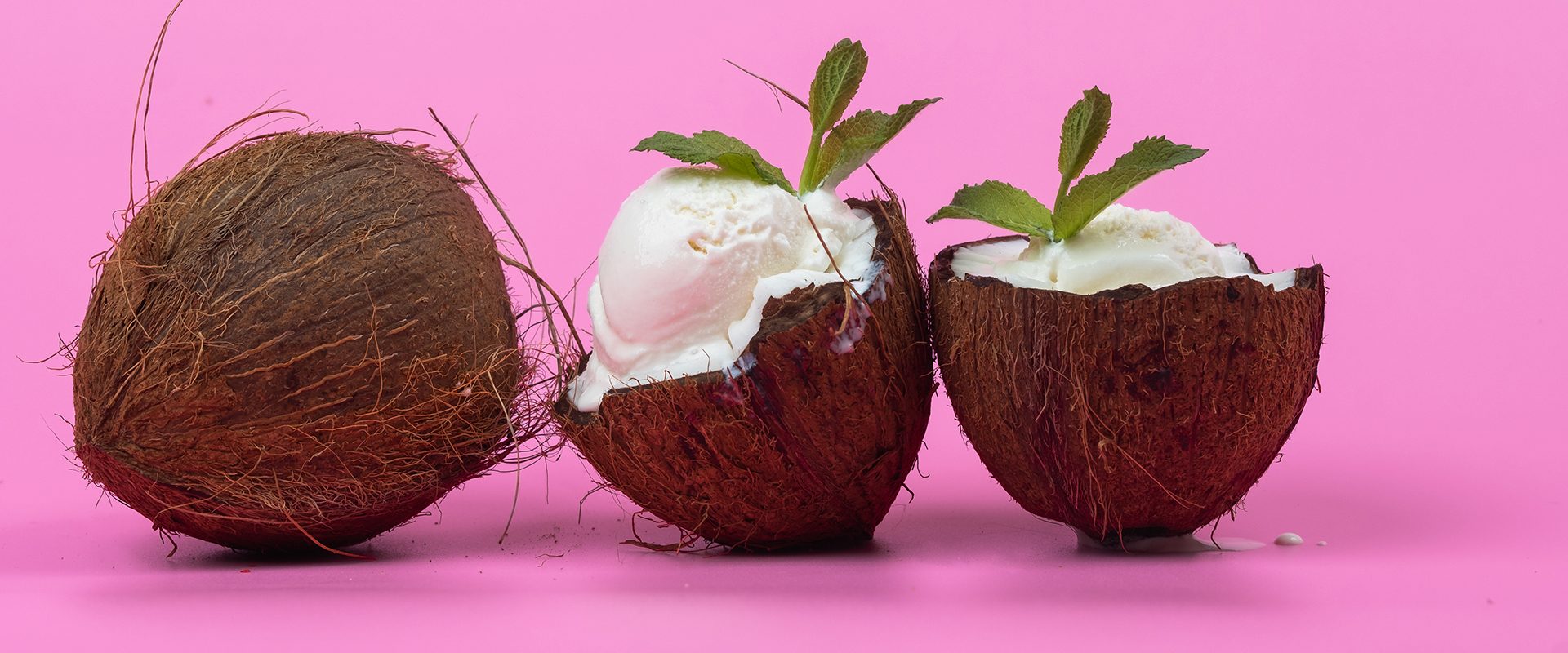 Vanilla ice cream balls in fresh coconut halves decorated with mint leaves on a pink background.